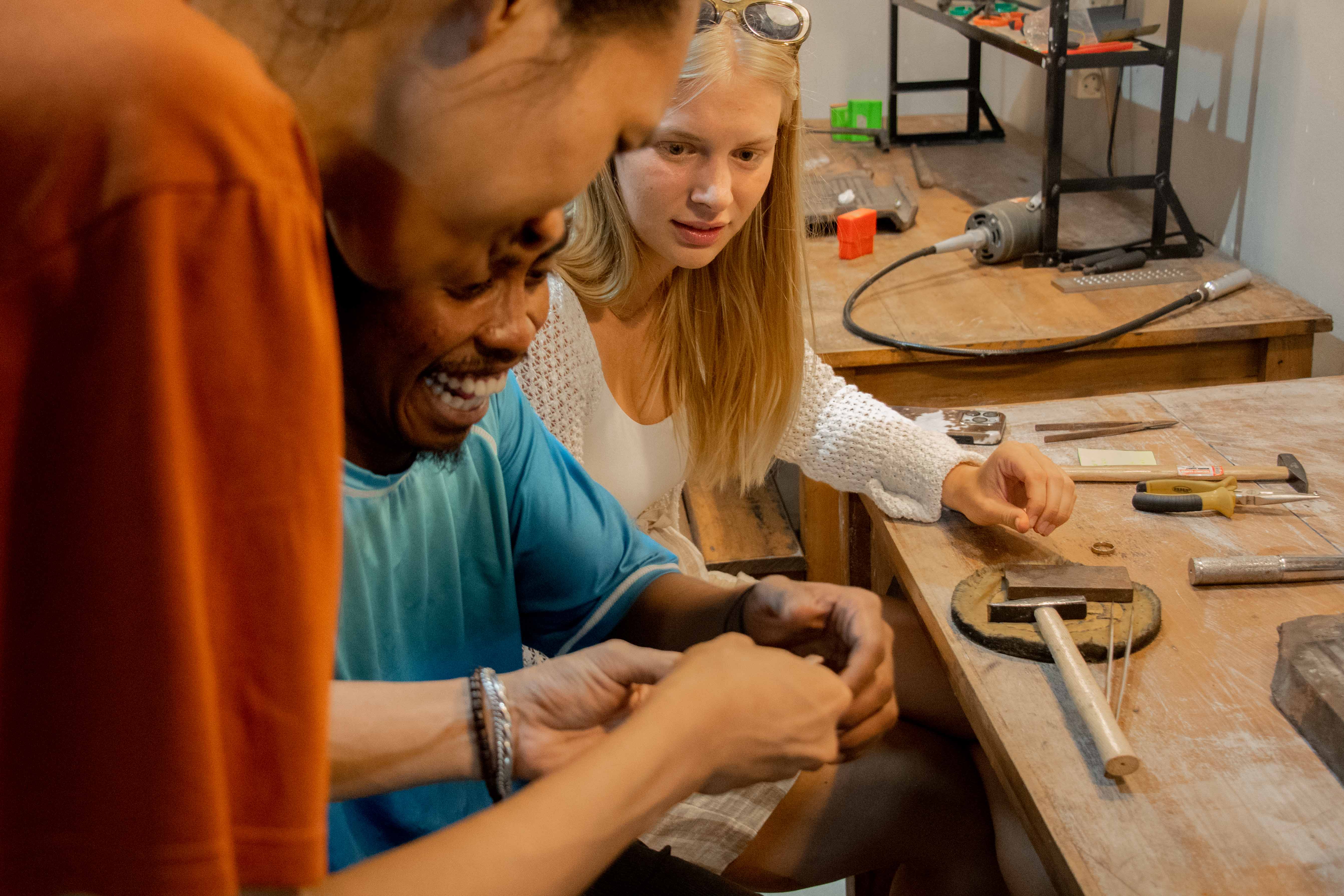 A guest and jewelry maker working together at a wooden workbench